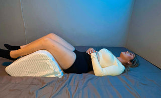 Woman resting on a bed using a leg elevation wedge pillow for comfortable sleep and ease back tension