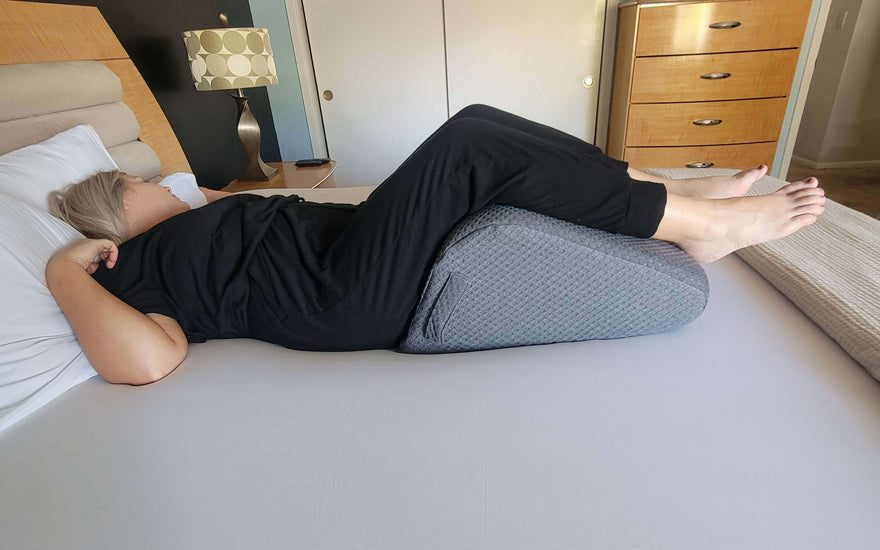 Woman resting on a bed using a leg elevation wedge pillow for comfortable sleep and posture alignment